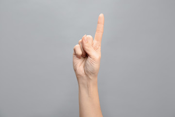 Woman showing number one on grey background, closeup. Sign language
