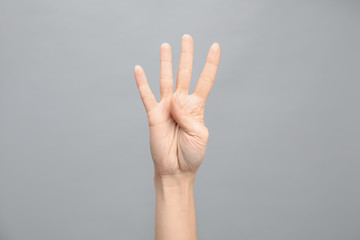 Woman showing number four on grey background, closeup. Sign language