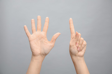 Woman showing sign six on grey background, closeup. Body language