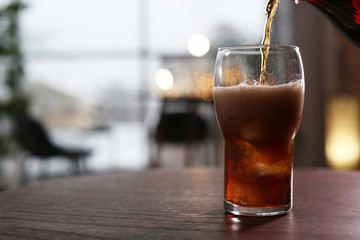 Pouring cola into glass on table against blurred background. Space for text