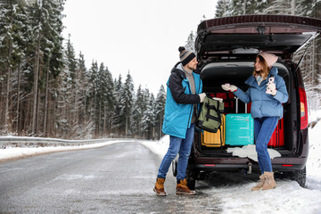 Naklejka premium Couple near open car trunk full of luggage on road, space for text. Winter vacation