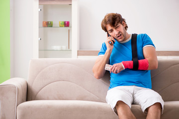 Young man with injured arm sitting on the sofa 