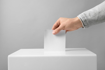 Man putting his vote into ballot box on light background, closeup