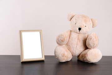 Photo frame with space for text and adorable teddy bear on table against light background. Child room elements