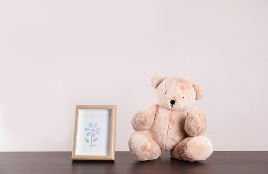 Adorable teddy bear and frame with cute picture on table against light background, space for text. Child room elements