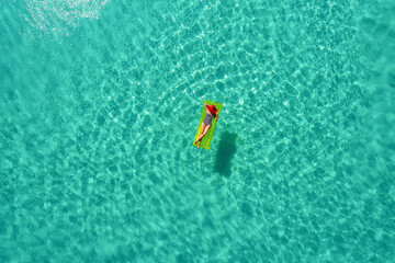 Aerial view of slim woman swimming on the swim mattress in the transparent turquoise sea in Seychelles. Summer seascape with girl, beautiful waves, colorful water. Top view from drone