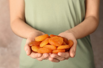 Woman holding handful of dried apricots on color background, closeup. Healthy fruit