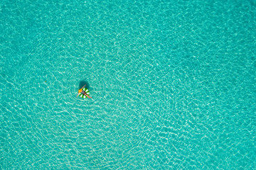 Aerial view of slim woman swimming on the swim ring  donut in the transparent turquoise sea in Seychelles. Summer seascape with girl, beautiful waves, colorful water. Top view from drone