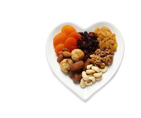 Heart shaped plate with different dried fruits and nuts on white background, top view. Space for text