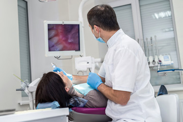 Dentist checking patient's teeth with camera, looking on screen