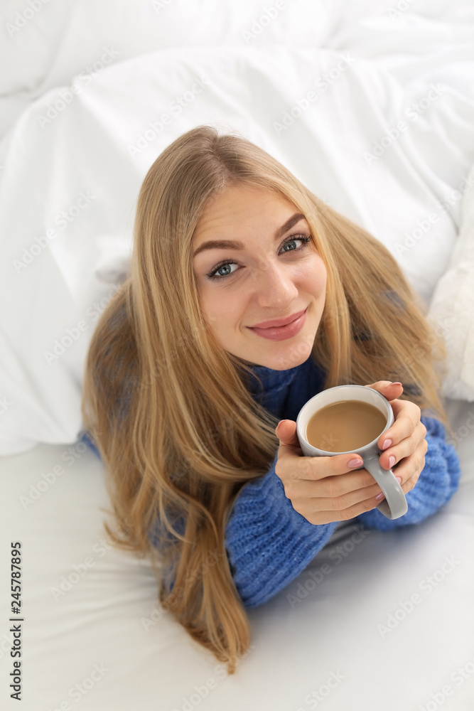 Sticker Beautiful young woman with cup lying in bed at home. Winter atmosphere