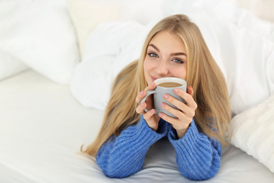 Beautiful young woman lying with cup in bed at home. Winter atmosphere
