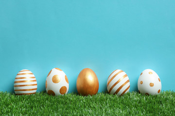 Line of traditional Easter eggs decorated with golden paint on green lawn against color background, space for text