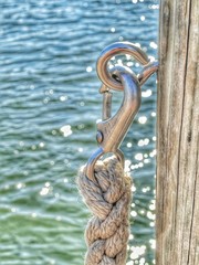 braided nautical rope with metal clip anchored to wooden dock mooring with glistening blue green water