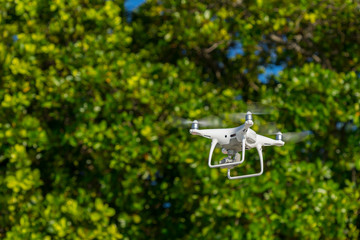 Drone in flight, green trees in the background, selective focus on the drone.