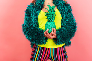 Pop art fashion girl with pineapple turquoise in the hands on a pink background. coat semi fur and tights