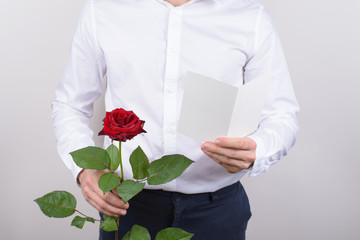 Cropped close up photo of cheerful handsome smiling sincere falling in love guy opening his heart to beloved lady reading poem holding card post card in hands isolated grey background