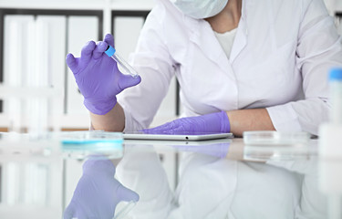 Close-up of professional female scientist in protective eyeglasses making experiment with reagents in laboratory or making blood tests. Medicine, science and research concept