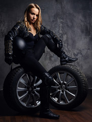 Fototapeta na wymiar Fashion, sport, extreme. Beautiful woman wearing racer uniform, posing in a studio while sitting on a wheel and holding a protective helmet.