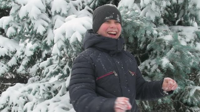 Happy child boy plays with snowy fir tree branches, winter forest, beautiful landscape
