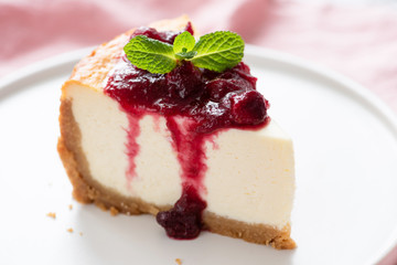 Cheesecake with sweet cherry sauce on plate decorated with mint leaf. Closeup view. Slice of tasty cake