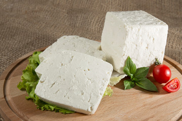 White cheese with some garnitures such as lettuce, a slice of cherry tomato and bassil on a wooden plate with sackcloth table sheet