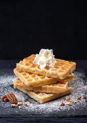 Close-up of sweet tasty Belgian waffles, sprinkled with powdered sugar, pecans, with whipped cream - obrazy, fototapety, plakaty