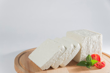 White cheese with some garnitures such as lettuce, cherry tomato slice and basil on a wooden plate, white background
