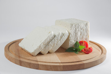 White cheese with some garnitures such as lettuce, cherry tomato slice and basil on a wooden plate, white background