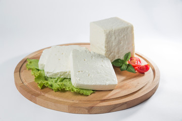 White cheese with some garnitures such as lettuce, cherry tomato slice and basil on a wooden plate, white background