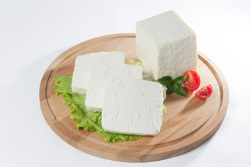White cheese with some garnitures such as lettuce, cherry tomato slice and basil on a wooden plate, white background