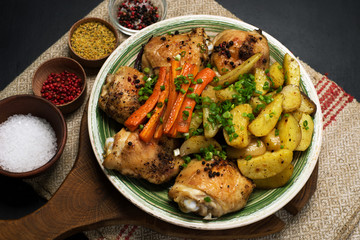 Baked chicken legs with potatoes and carrots under spices and seasonings