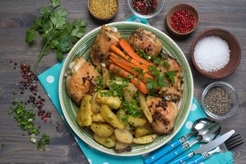 Baked chicken legs with potatoes and carrots under spices and seasonings