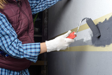 female painting a wall with masking tape and roller