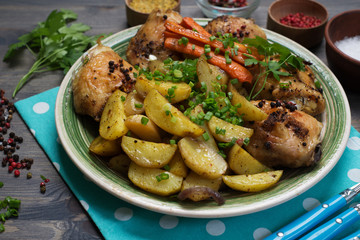 Baked chicken legs with potatoes and carrots under spices and seasonings. Close-up, selective sharpness