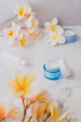 Obraz na płótnie Canvas group of skincare products including moisturiser scrub and hand cream pots on marble table with exotic frangipani flowers