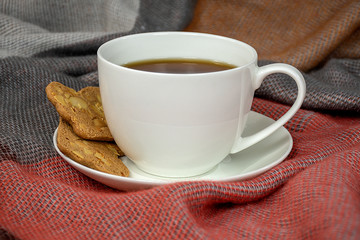 close up of black coffee in white cup on saucer with cookies and warm blanket
