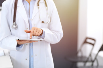 Female physician using digital tablet  while standing near reception desk at clinic or emergency hospital. Unknown doctor woman at work. Medicine concept
