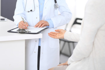 Unknown doctor and  female patient  discussing something while standing near reception desk in emergency hospital. Physician at work in clinic. Medicine and health care concept