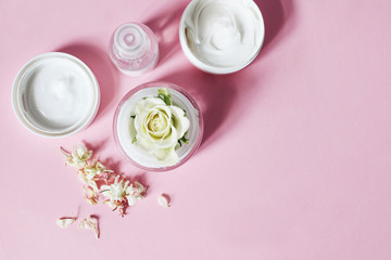 Sunny beauty composition. Closeup of skin cream, tonicum bottle, dry flowers and rose with long shadows. Pink background. Organic cosmetics, spa concept. Empty space, flat lay, top view.