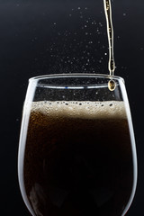 Glass of pouring fizzy drink with ice on a black background