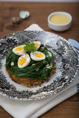 Quail eggs with spinach and rosti on wooden background, close view