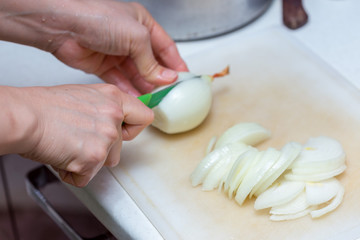 Obraz na płótnie Canvas Girl's hand with a knife cutting onions on wooden Board