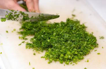 Female hands chopping the dill leaves on a cutting board with a knife. The concept of cooking