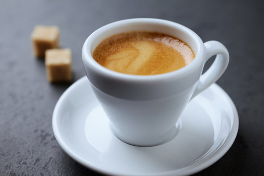 Cup of coffee and two brown sugar cubes on black stone background. Close up. 