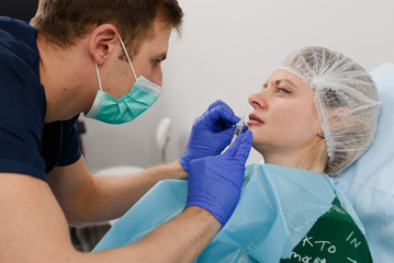 girl do plastic operation in medical clinic; doctor does lip augmentation surgery; injecting...