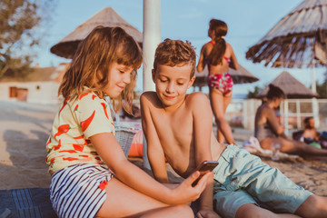 Fototapeta na wymiar Children playing with mobile phone on sandy beach