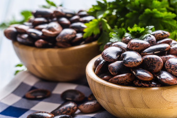 Uncooked beans in wooden bowles  with parsley herbs on kitchen table