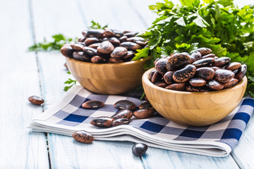 Uncooked beans in wooden bowles  with parsley herbs on kitchen table