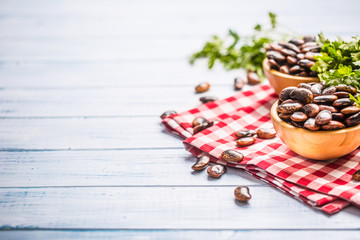 Uncooked beans in wooden bowles  with parsley herbs on kitchen table